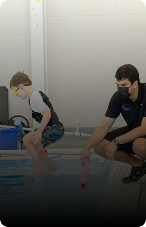 A boy and instructor practicing swimming techniques on the poolside.
