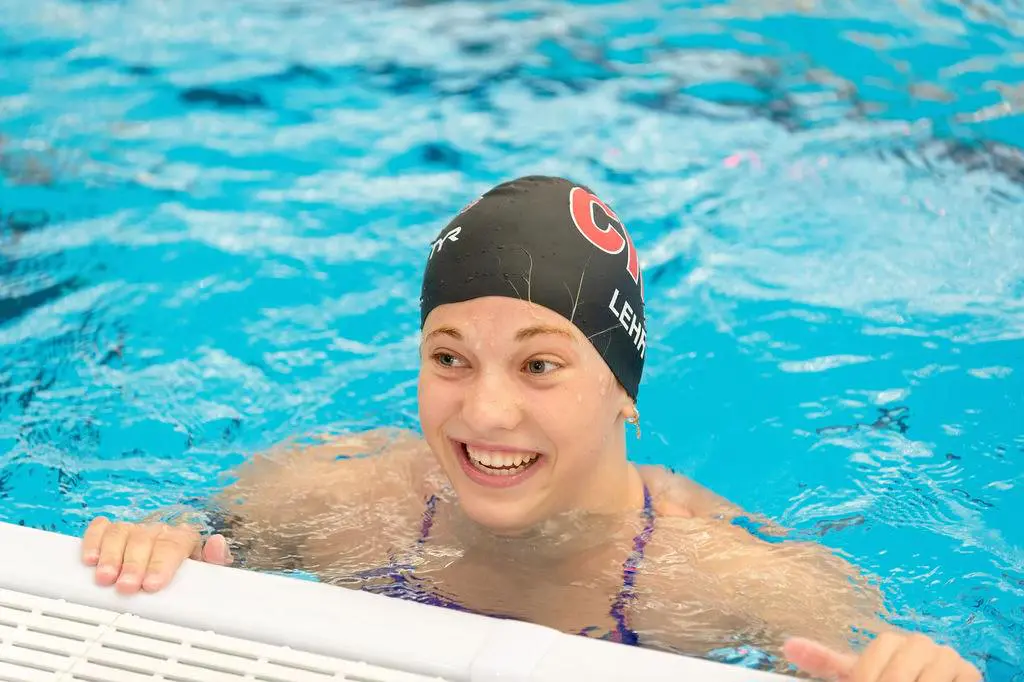 A young swimmer smiling in a pool wearing a swim cap.