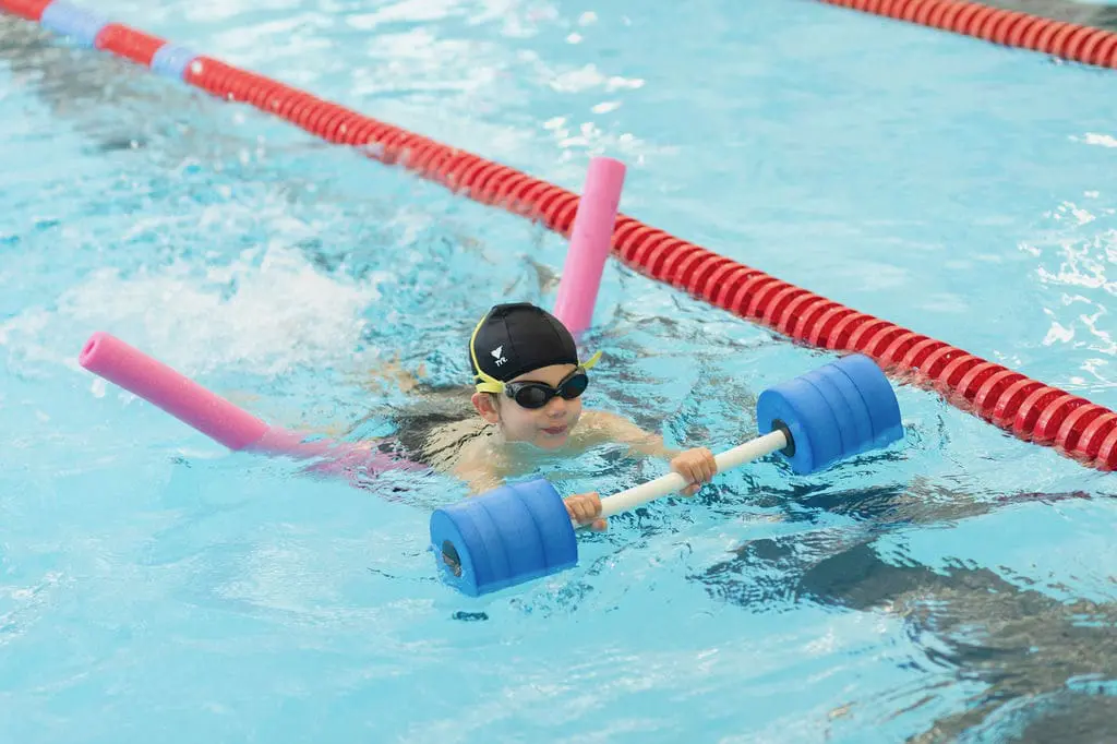 Child swimming with foam dumbbell and noodle