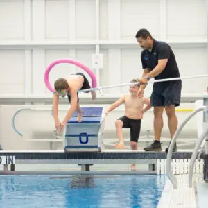 Child diving into pool with instructor's support.