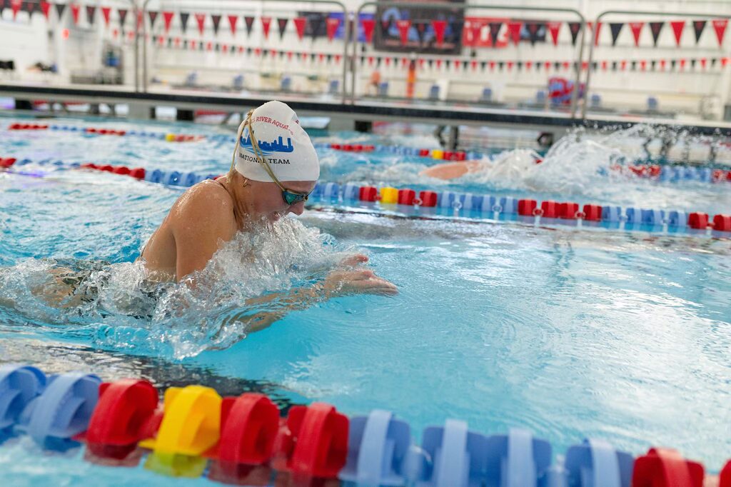 Young swimmer competing in a pool race wearing a swim cap and goggles.