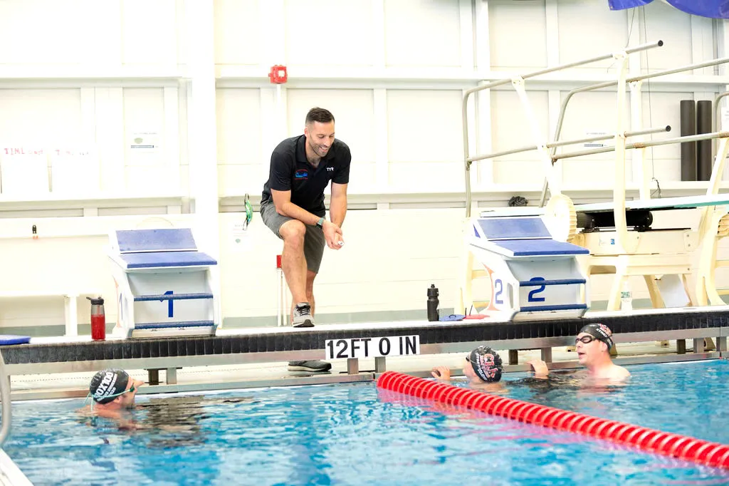 A coach watches swimmers practicing in a pool.