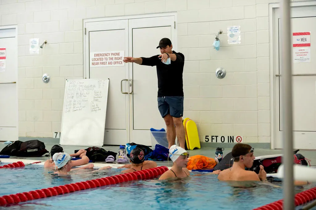 A swim instructor guides two children in a pool.