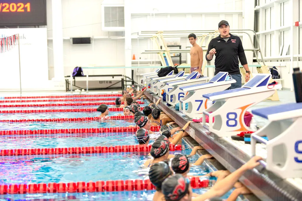 Swimmers line up at the pool edge, ready for a swimming competition start.