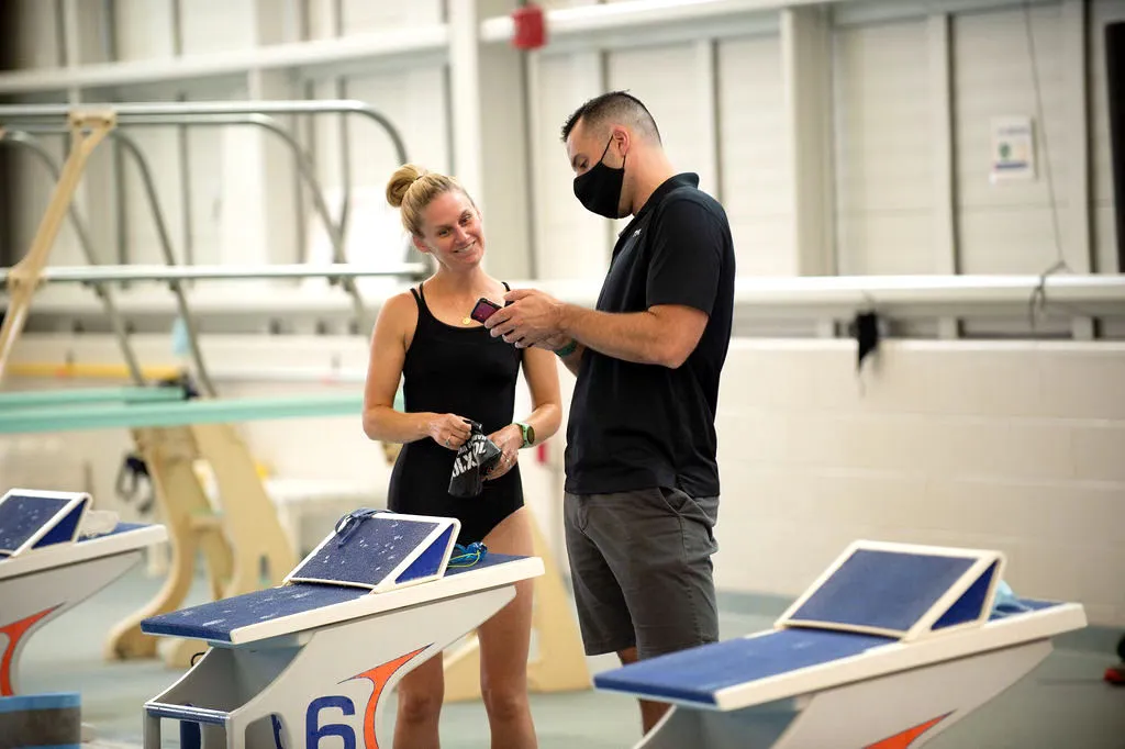 Two people in a sports setting, one wearing a mask, looking at a phone.